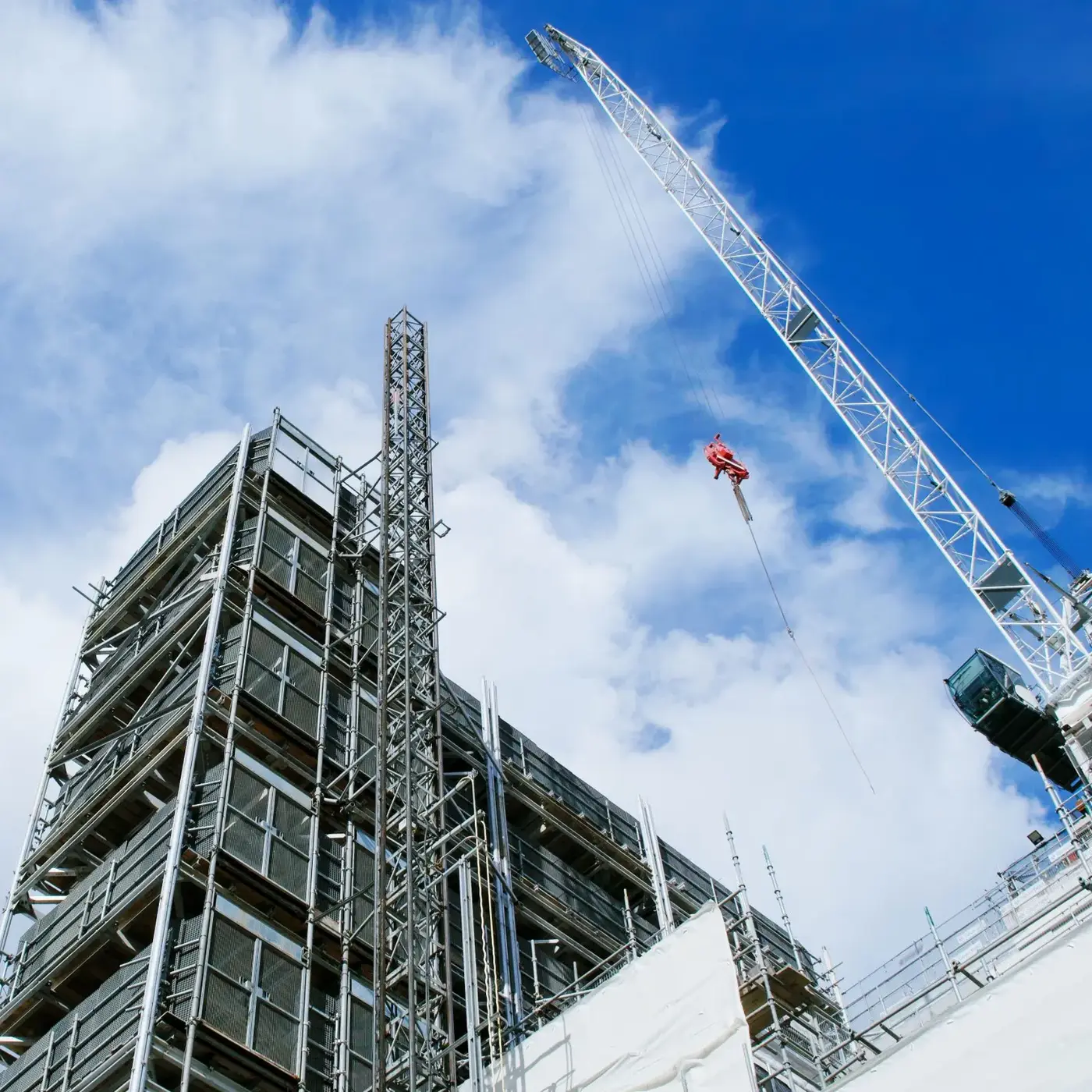 Tower crane beside a high-rise building under construction against a blue sky